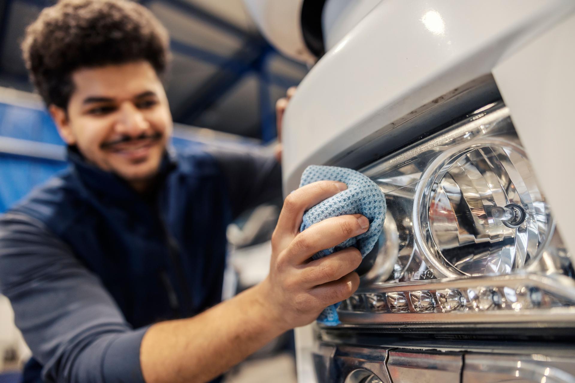 Close up of multicultural worker's hand with microfiber cloth cleaning headlight on vehicle.